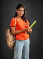Beautiful young girl with a backpack standing and holding a notebook, posing on a grey background. photo