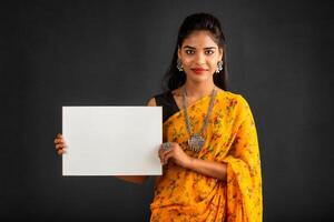 A young girl or businesswoman wearing a saree and holding a signboard in her hands on a gray background. photo