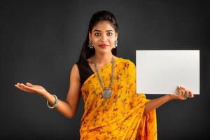 A young girl or businesswoman wearing a saree and holding a signboard in her hands on a gray background. photo
