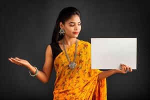 A young girl or businesswoman wearing a saree and holding a signboard in her hands on a gray background. photo