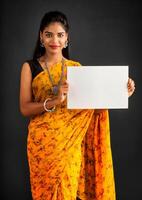 A young girl or businesswoman wearing a saree and holding a signboard in her hands on a gray background. photo