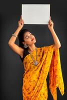 A young girl or businesswoman wearing a saree and holding a signboard in her hands on a gray background. photo