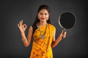 Young girl holding and posing with kitchen utensils pan on a grey background photo