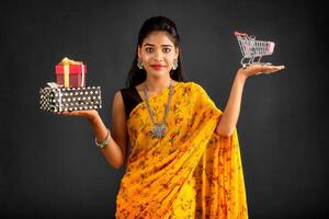 Beautiful young girl or woman holding and posing with a miniature trolley shopping cart and gift box on a gray background photo