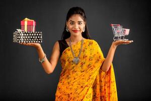 Beautiful young girl or woman holding and posing with a miniature trolley shopping cart and gift box on a gray background photo