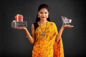 Beautiful young girl or woman holding and posing with a miniature trolley shopping cart and gift box on a gray background photo