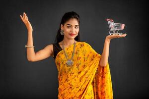 Happy young Smiling girl with a miniature trolley shopping cart on the gray background. Beautiful girl in shopping concept. photo