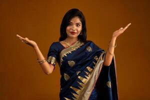 Portrait of Indian traditional young woman or girl presenting something, showing copy space on her palm on a brown background photo