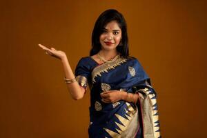 Portrait of Indian traditional young woman or girl presenting something, showing copy space on her palm on a brown background photo