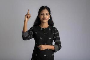 Young smiling girl pointing fingers to copy space on a grey background photo