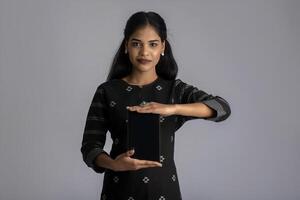 Young beautiful woman holding and showing blank screen of smartphone or mobile or tablet phone on a gray background. photo