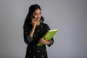 Pretty young girl holding book and using mobile on grey background photo