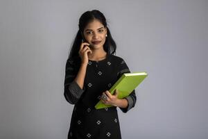 Pretty young girl holding book and using mobile on grey background photo