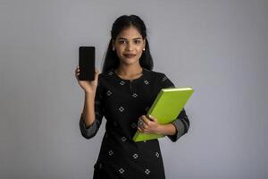 Pretty young girl holding book and using mobile on grey background photo