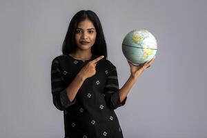 young girl holding the world globe and posing on a grey background. photo