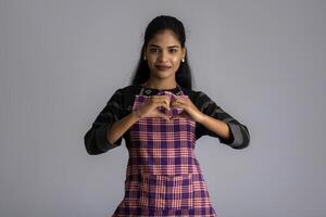 Portrait of Indian woman chef or cook in an apron, presenting, pointing, with ok sign, thumbs up on the grey background. photo