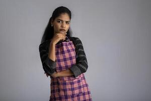 Portrait of Indian woman chef or cook in an apron, presenting, pointing, with ok sign, thumbs up on the grey background. photo