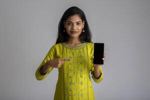 Young beautiful girl holding and showing blank screen of smartphone or mobile or tablet phone on a gray background. photo