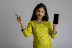 Young beautiful girl holding and showing blank screen of smartphone or mobile or tablet phone on a gray background. photo