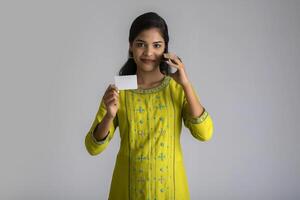 Young smiling beautiful woman or girl presenting credit card while using mobile or smartphone on grey background. photo