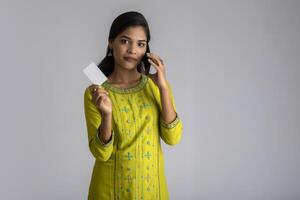Young smiling beautiful woman or girl presenting credit card while using mobile or smartphone on grey background. photo