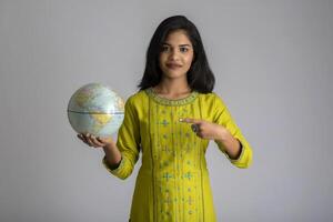 young girl holding the world globe and posing on a grey background. photo