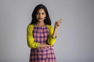 Portrait of Indian woman chef or cook in an apron, presenting, pointing, with ok sign, thumbs up on the grey background. photo