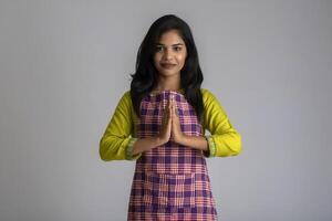 Portrait of Indian woman chef or cook in an apron, presenting welcome expression inviting, greeting Namaste on grey background. photo