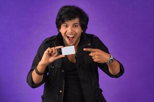 Young smiling handsome man posing with a credit card on purple background. photo