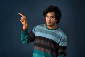 Portrait of a successful cheerful young man pointing and presenting something with hand or finger with a happy smiling face. photo