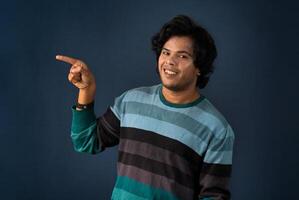 Portrait of a successful cheerful young man pointing and presenting something with hand or finger with a happy smiling face. photo