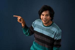 Portrait of a successful cheerful young man pointing and presenting something with hand or finger with a happy smiling face. photo