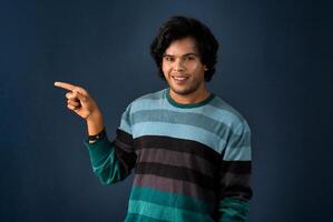 Portrait of a successful cheerful young man pointing and presenting something with hand or finger with a happy smiling face. photo