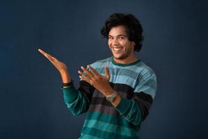 Portrait of a successful cheerful young man pointing and presenting something with hand or finger with a happy smiling face. photo