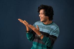 Portrait of a successful cheerful young man pointing and presenting something with hand or finger with a happy smiling face. photo