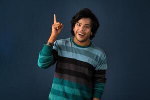 Portrait of a successful cheerful young man pointing and presenting something with hand or finger with a happy smiling face. photo