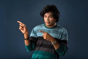 Portrait of a successful cheerful young man pointing and presenting something with hand or finger with a happy smiling face. photo