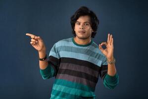 Portrait of a successful cheerful young man pointing and presenting something with hand or finger with a happy smiling face. photo