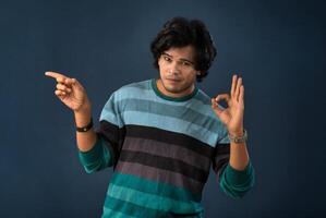 Portrait of a successful cheerful young man pointing and presenting something with hand or finger with a happy smiling face. photo