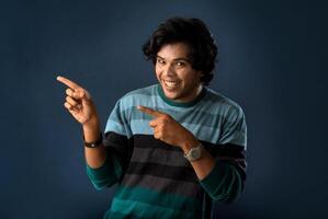 Portrait of a successful cheerful young man pointing and presenting something with hand or finger with a happy smiling face. photo