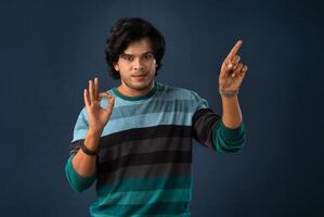 Portrait of a successful cheerful young man pointing and presenting something with hand or finger with a happy smiling face. photo