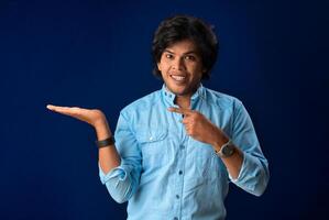Portrait of a successful cheerful young man holding and presenting something on hand with a happy smiling face. photo