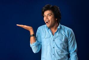 Portrait of a successful cheerful young man holding and presenting something on hand with a happy smiling face. photo