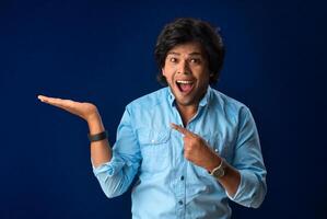 Portrait of a successful cheerful young man holding and presenting something on hand with a happy smiling face. photo
