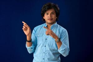 Portrait of a successful cheerful young man pointing and presenting something with hand or finger with a happy smiling face. photo