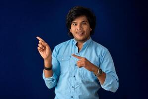 Portrait of a successful cheerful young man pointing and presenting something with hand or finger with a happy smiling face. photo