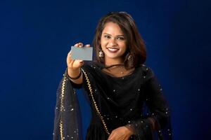 Young smiling beautiful girl posing with a credit or debit card on blue background. photo