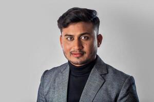 Portrait of Happy Indian young man, businessman wearing a blazer on grey background posing, satisfied successful male in formal suit photo