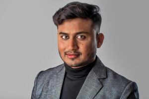 Portrait of Happy Indian young man, businessman wearing a blazer on grey background posing, satisfied successful male in formal suit photo