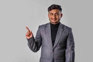 Portrait of a successful cheerful young man wearing formal suit pointing and presenting something with hand or finger with a happy smiling face. photo